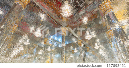 Mirror mosaic ceiling inside a temple with multiple light fixtures creating a reflective surface that forms bright patterns and detailed architectural design. 137892431