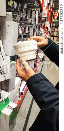 A customer holds a paint tray and brushes while shopping in a hardware store aisle. Concepts of home improvement, DIY renovation, consumer choice, and retail shopping behavior. A customer holds a paint tray and brushes while shopping in a hardware store aisle. Concepts of home improvement, DIY renovation, consumer choice, and retail shopping behavior. 137892859
