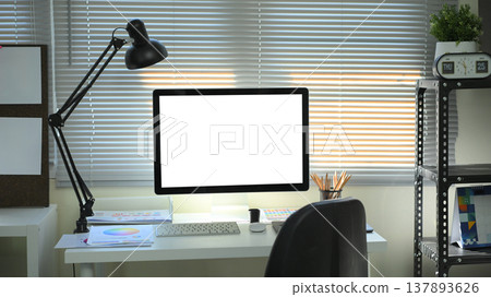 Modern designer workspace with blank computer screen, desk lamp, color charts, and stationery in a creative office Modern designer workspace with blank computer screen, desk lamp, color charts, and stationery in a creative office 137893626