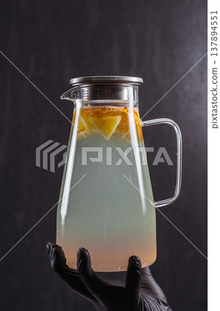 Clear Glass Pitcher Citrus Slices Held Blackgloved Hand, Moody Studio Lighting, Subtle Condensation Clear Glass Pitcher Citrus Slices Held Blackgloved Hand, Moody Studio Lighting, Subtle Condensation 137894551