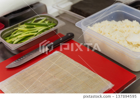 Sushi Rolling Station With Bamboo Mat, Sharp Knife And Cucumber Strips On Red Board, Layout Ready 137894595