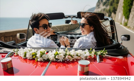 Happy Asian couple celebrating wedding in red convertible car decorated with white flowers on coastal road 137894942