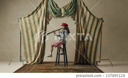 Young girl playing clarinet sitting on stool in studio with vintage curtains. Young girl playing clarinet sitting on stool in studio with vintage curtains. 137895128