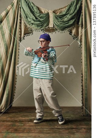 Young boy playing violin in studio with vintage curtains expressive performance. Young boy playing violin in studio with vintage curtains expressive performance. 137895136