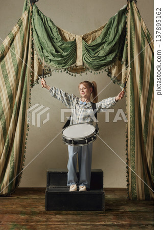 Little girl playing snare drum with raised sticks celebrating music performance. Little girl playing snare drum with raised sticks celebrating music performance. 137895162