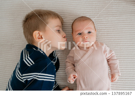 Older brother kissing newborn baby. Emotional moment of sibling love, tenderness and protection in family life. Older brother kissing newborn baby. Emotional moment of sibling love, tenderness and protection in family life. 137895167