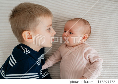 Older brother lying next to newborn baby. Tender sibling bonding moment showing curiosity, love and first interaction between children. 137895172