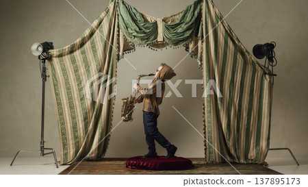 Little boy playing saxophone on small stage dramatic performance childhood music Little boy playing saxophone on small stage dramatic performance childhood music 137895173