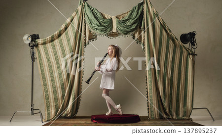 Little girl playing clarinet on stage side view expressive childhood music performance. 137895237