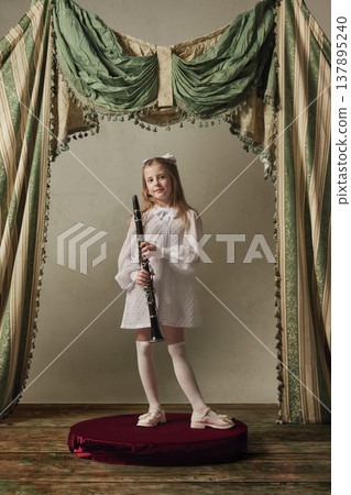 Little girl holding clarinet on stage in white dress childhood music learning. 137895240