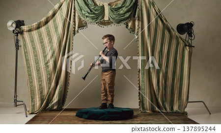 Little boy playing clarinet on small classical stage with curtains. 137895244