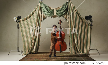Little boy holding cello on performance stage with studio lights. 137895253
