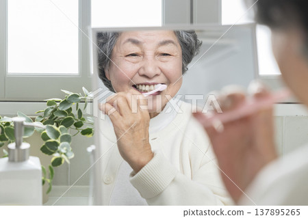 Senior woman brushing her teeth while looking in the mirror Senior woman brushing her teeth while looking in the mirror 137895265