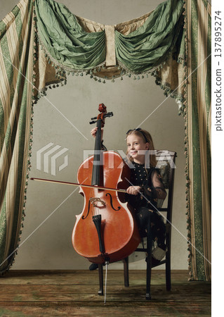 Little girl playing cello on vintage stage with draped curtains. 137895274
