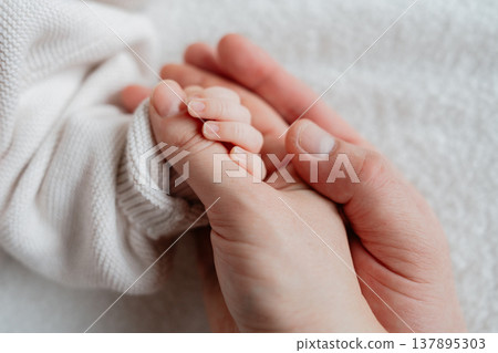 Newborn baby holding an adult finger in a soft, neutral setting. Emotional close-up symbolizing trust, safety, and family connection. Newborn baby holding an adult finger in a soft, neutral setting. Emotional close-up symbolizing trust, safety, and family connection. 137895303