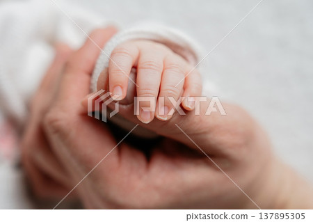 Newborn baby holding parent finger in close-up. Emotional moment of trust and connection. Concept of family bonding, care and unconditional love in early childhood. Newborn baby holding parent finger in close-up. Emotional moment of trust and connection. Concept of family bonding, care and unconditional love in early childhood. 137895305