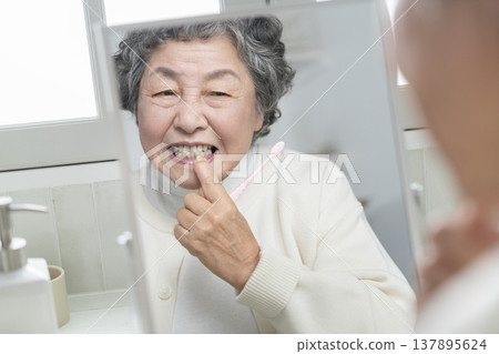 A senior woman becomes concerned about her gums while brushing her teeth. 137895624