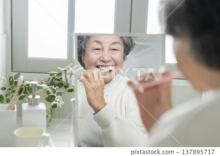 An 80-year-old woman brushing her teeth while looking in the mirror. An 80-year-old woman brushing her teeth while looking in the mirror. 137895717