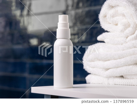 White spray cosmetic bottle near white bath towel in dark blue bathroom, cosmetic mockup 137896559