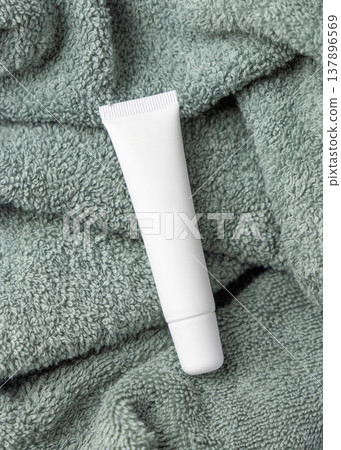 White blank cream tube mockup on sage green bath towel top view. Unbranded cosmetic packaging White blank cream tube mockup on sage green bath towel top view. Unbranded cosmetic packaging 137896569