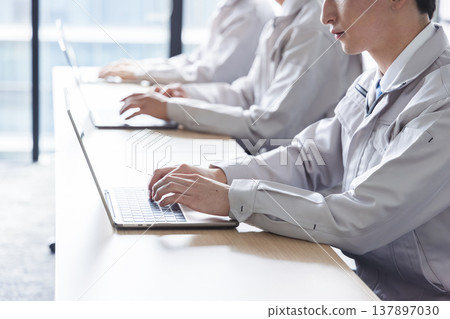 A young man in work clothes operating a computer. A young man in work clothes operating a computer. 137897030