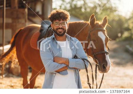 Smiling, arms crossed. Guy is with horse on the farm Smiling, arms crossed. Guy is with horse on the farm 137897164