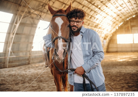 In casual clothes, standing by. Man is with horse in the hangar In casual clothes, standing by. Man is with horse in the hangar 137897235