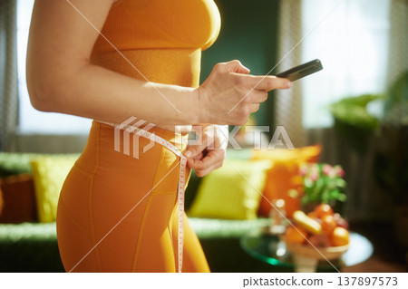 Woman Tracking Fitness Progress with Phone and Measuring Tape Woman Tracking Fitness Progress with Phone and Measuring Tape 137897573