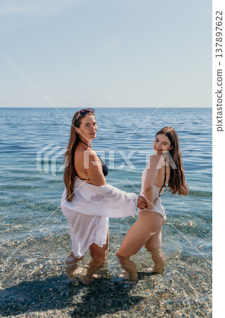 Beach women vacation Two women in swimwear and white shirt standing in clear sea water under blue sky during summer vacation holiday 137897622