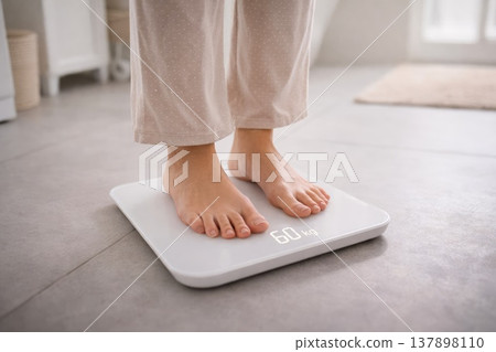 Close up of woman standing on digital bathroom scale measuring body weight at home Close up of woman standing on digital bathroom scale measuring body weight at home 137898110