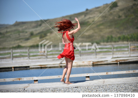 Back view of woman with red hair in red dress by pool Back view of woman with red hair in red dress by pool 137898410