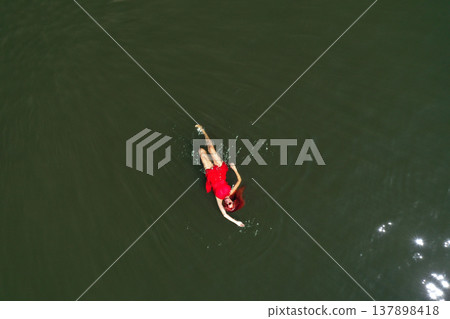 Aerial view of woman in red dress floats peacefully in a lake, embracing serenity and solitude 137898418