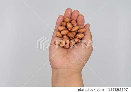 A close-up of a peanut held in the palm of a hand against a white background. A close-up of a peanut held in the palm of a hand against a white background. 137898507