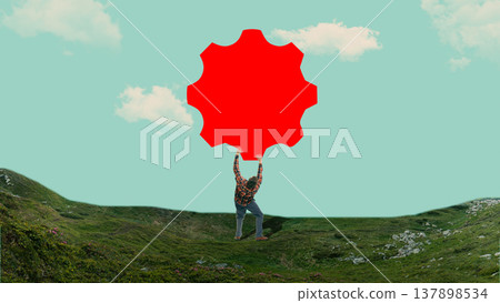 Man standing on mountain landscape holding oversized gear shape against sky background. 137898534
