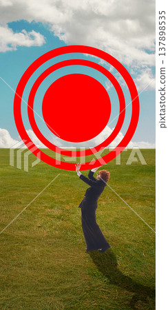 Man standing on grass holding oversized target sign against cloudy sky background. 137898535