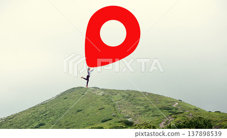 Woman on mountain hill holding oversized red map pin location marker against neutral sky. 137898539