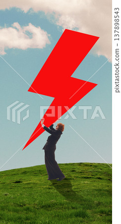 Businessman standing on grassy hill holding oversized red lightning bolt shape against cloudy sky. Businessman standing on grassy hill holding oversized red lightning bolt shape against cloudy sky. 137898543
