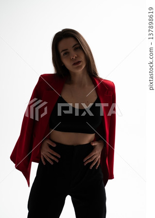 Young brunette woman striking a confident pose, embodying business style and female empowerment, wearing a red blazer and black crop top in a studio setting 137898619