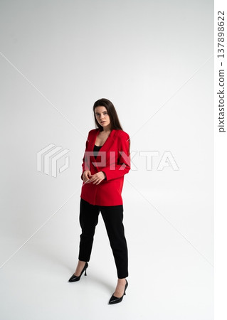 Young businesswoman posing in a powerful red blazer and black trousers, embodying confidence, corporate professionalism, and fashion in a studio setting Young businesswoman posing in a powerful red blazer and black trousers, embodying confidence, corporate professionalism, and fashion in a studio setting 137898622