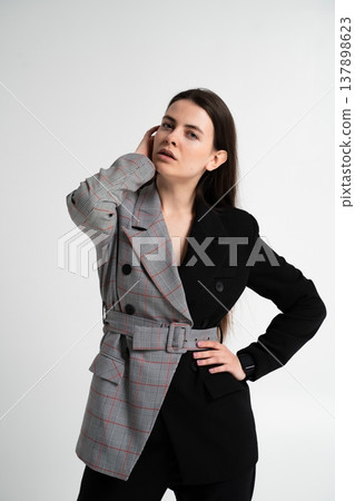 Fashionable woman posing in a studio, wearing a modern half plaid, half solid black double-breasted blazer, reflecting individuality, contrast, duality, and unique style 137898623