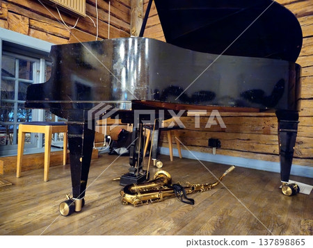 A tenor saxophone rests on the stage floor beneath a grand piano. 137898865