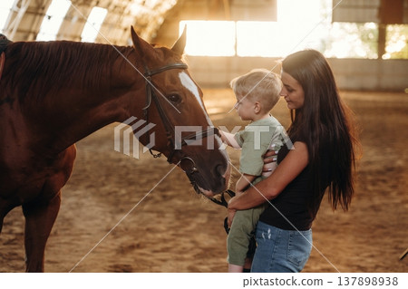 Curious kid is touching the animal. Mother and little son are with horse in hangar Curious kid is touching the animal. Mother and little son are with horse in hangar 137898938