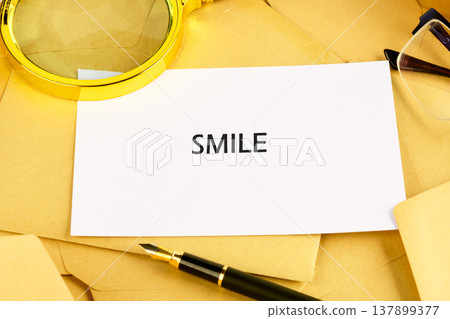 A white card with the word SMILE in bold black letters rests on golden envelopes A white card with the word SMILE in bold black letters rests on golden envelopes 137899377