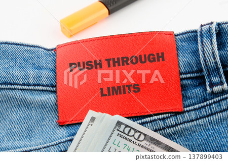 Red label on blue jeans: push limits, ambition. USD bills and yellow highlighter nearby 137899403