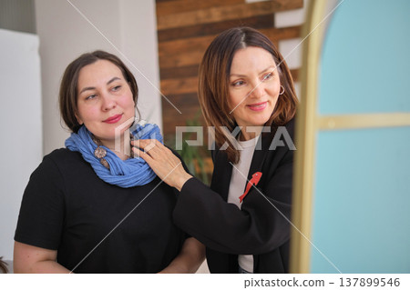 fashion consultation, stylist skillfully adjusts a blue scarf client while adding bold necklace fashion consultation, stylist skillfully adjusts a blue scarf client while adding bold necklace 137899546