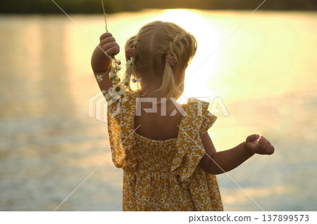 two-year-old cherub stares at tranquil lake, her silhouette framed against a watercolor sunset. With bouquet of daisies in hand. youthful curiosity and invaluable lessons nature offers to our children two-year-old cherub stares at tranquil lake, her silhouette framed against a watercolor sunset. With bouquet of daisies in hand. youthful curiosity and invaluable lessons nature offers to our children 137899573