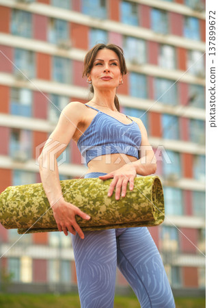 woman, dressed in blue athletic gear, stands tall with a yoga mat, exuding confidence and readiness for her workout. This photo emphasizes the ease of integrating fitness routines into a busy urban woman, dressed in blue athletic gear, stands tall with a yoga mat, exuding confidence and readiness for her workout. This photo emphasizes the ease of integrating fitness routines into a busy urban 137899672