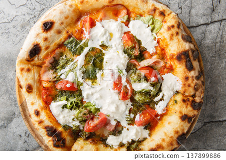 Crispy charred pizza with stracciatella cheese, pesto, ham and tomatoes close-up on a wooden board. Horizontal top view Crispy charred pizza with stracciatella cheese, pesto, ham and tomatoes close-up on a wooden board. Horizontal top view 137899886