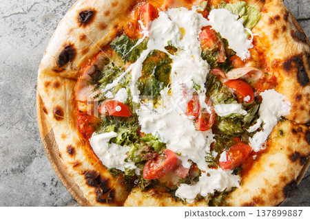 Close-up of neapolitan pizza with stracciatella cheese, pesto, ham and tomatoes on wooden board. top view from above Close-up of neapolitan pizza with stracciatella cheese, pesto, ham and tomatoes on wooden board. top view from above 137899887