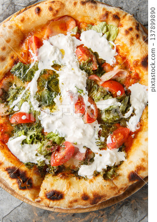 Pizza with stracciatella cheese, pesto, ham and tomatoes close-up on a wooden board. Vertical top view Pizza with stracciatella cheese, pesto, ham and tomatoes close-up on a wooden board. Vertical top view 137899890